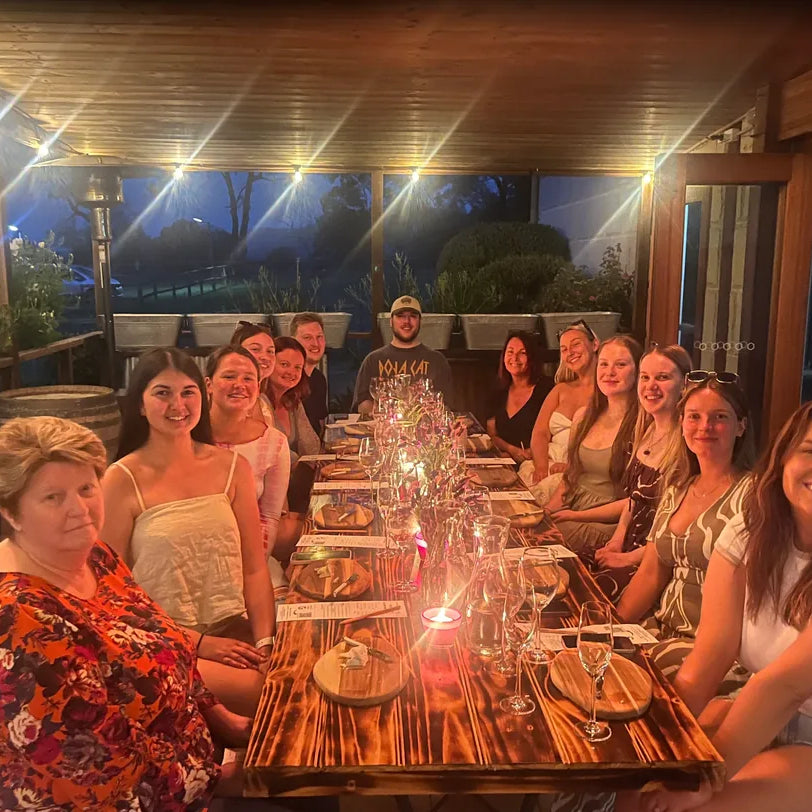 Guests seated at a long table for a private Unruly Wines tasting on a lit verandah at dusk