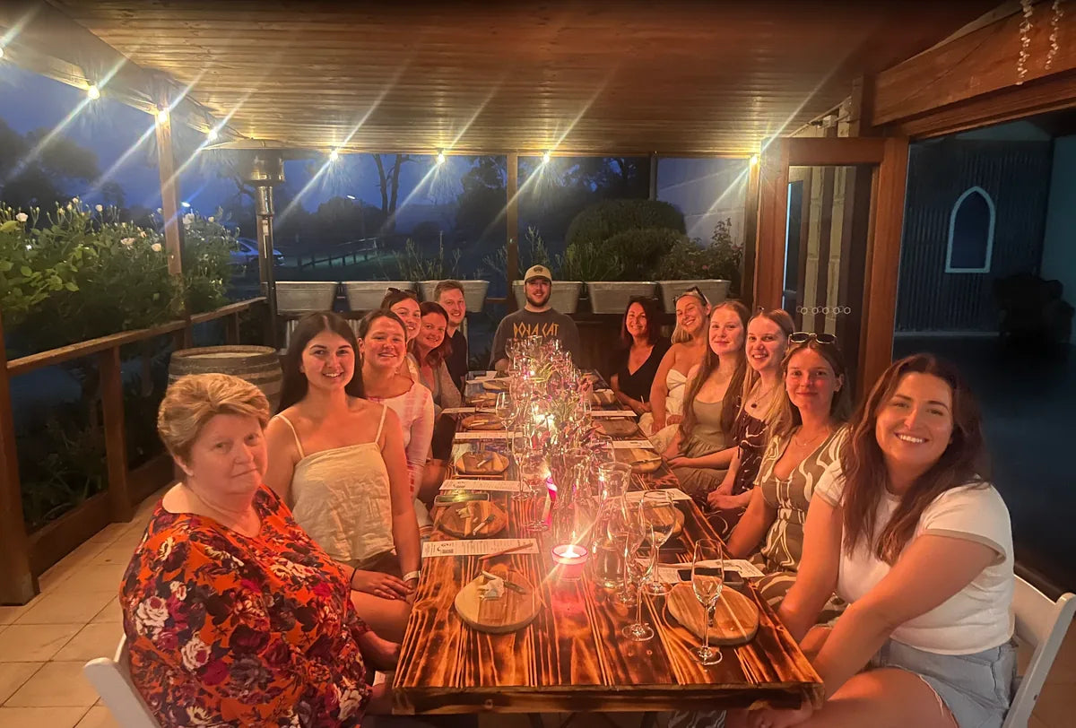 Guests seated at a long table for a private Unruly Wines tasting on a lit verandah at dusk