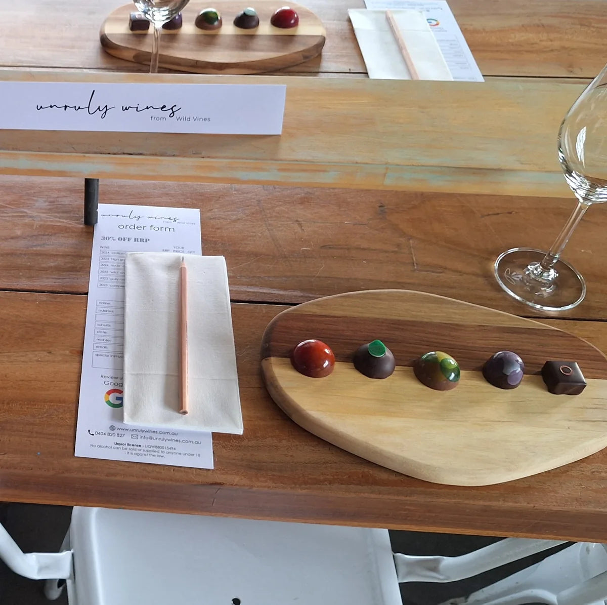 An Unruly Wines order form, glass and a board of hand painted chocolates set for a wine and chocolate tasting